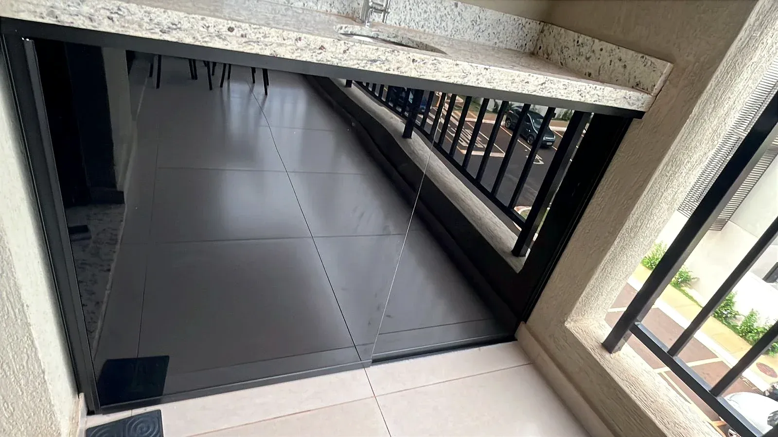 Portas de correr em vidro com película escura embaixo da bancada de granito da varanda
