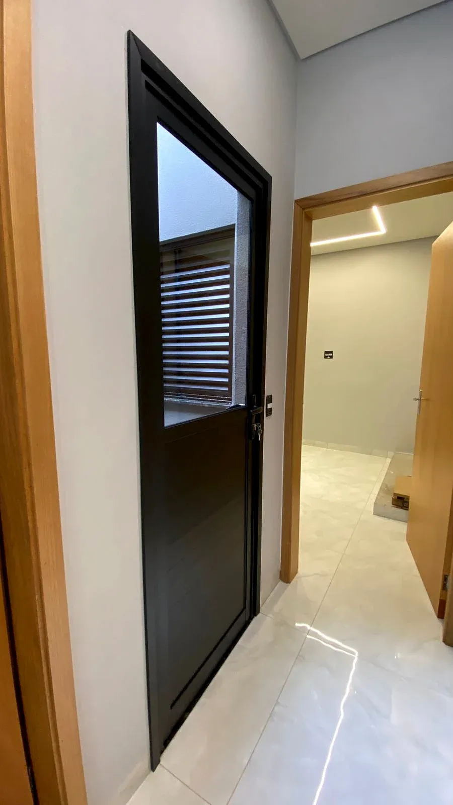 Porta em esquadria de alumínio preto com visor de vidro em corredor
